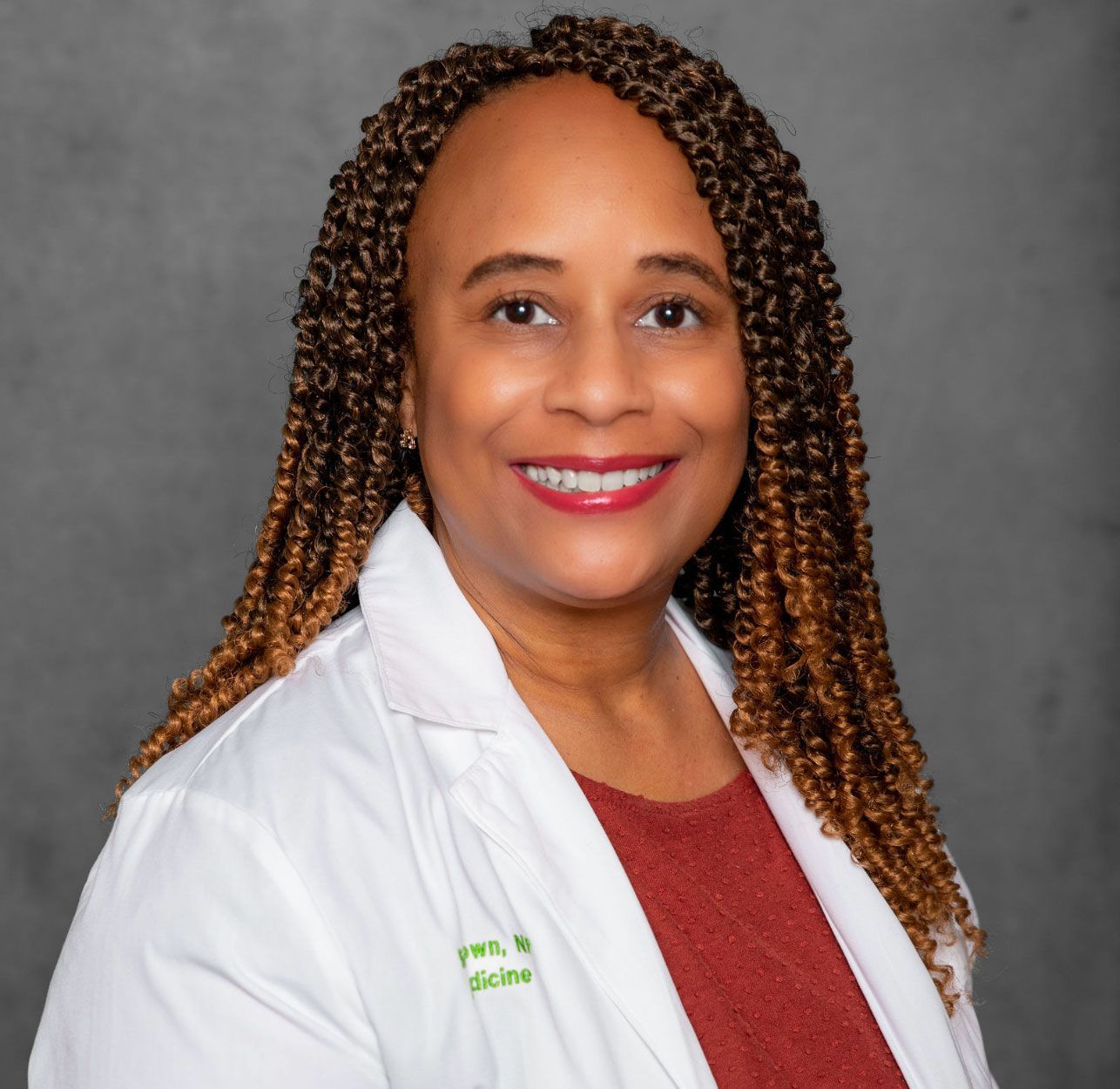 Professional headshot of a smiling person in a white coat over a red top against a gray background