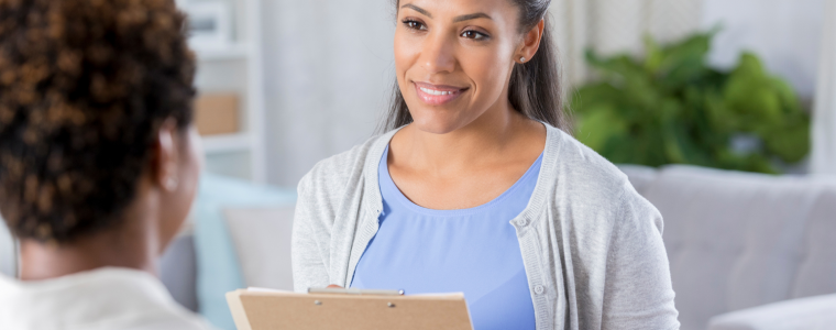 Two people talking in a bright office, one holding a clipboard and smiling.