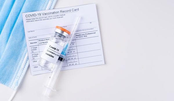 COVID-19 vaccination card, syringe, and face mask on a white surface