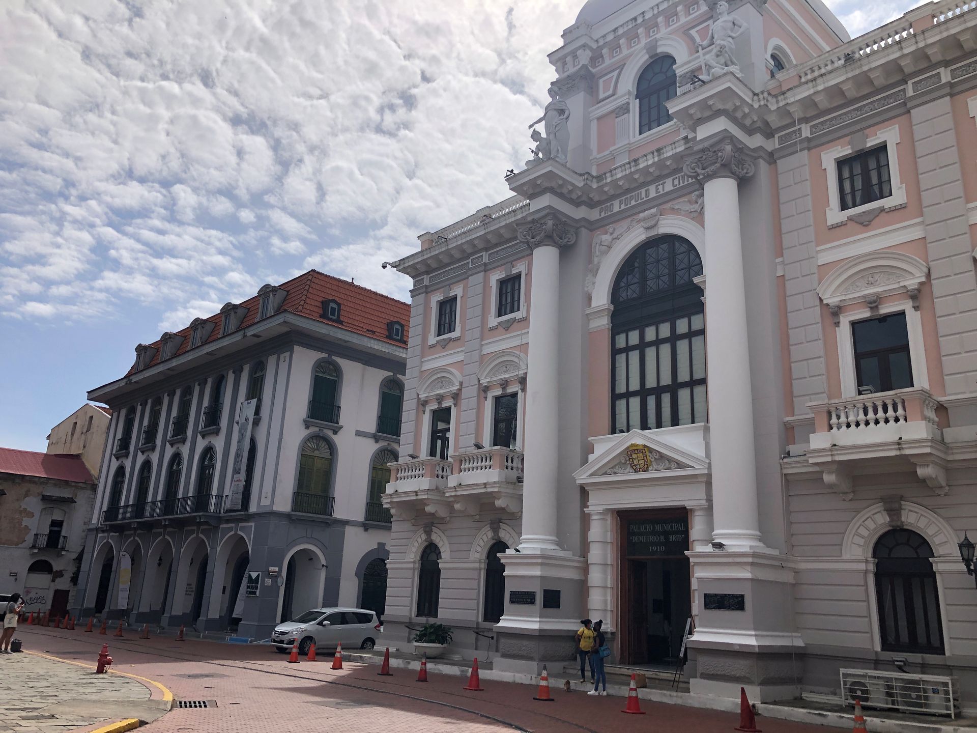 Elegant, light-colored buildings with ornate details; a sunny day. People near the entrance.