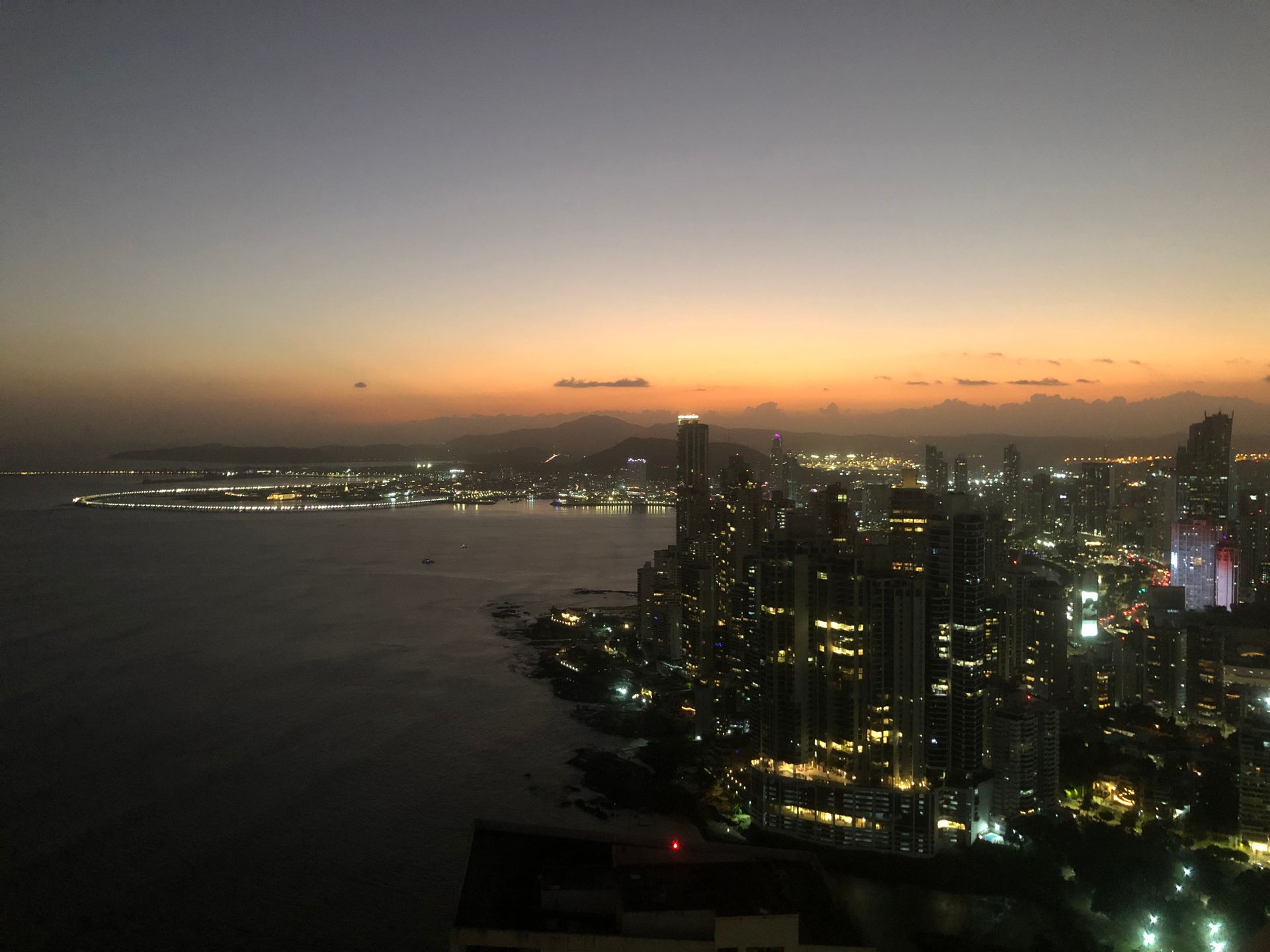 City skyline at dusk with lights reflecting on the water, orange and grey sky.
