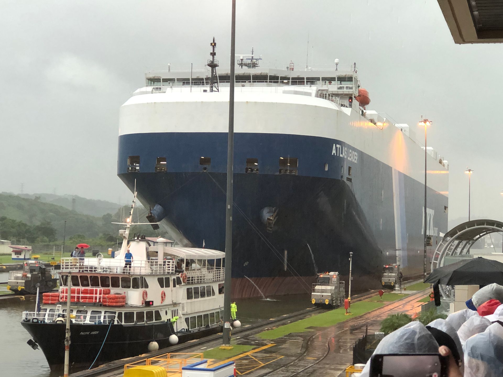 Large blue and white cargo ship in Panama Canal locks, with smaller boat alongside.