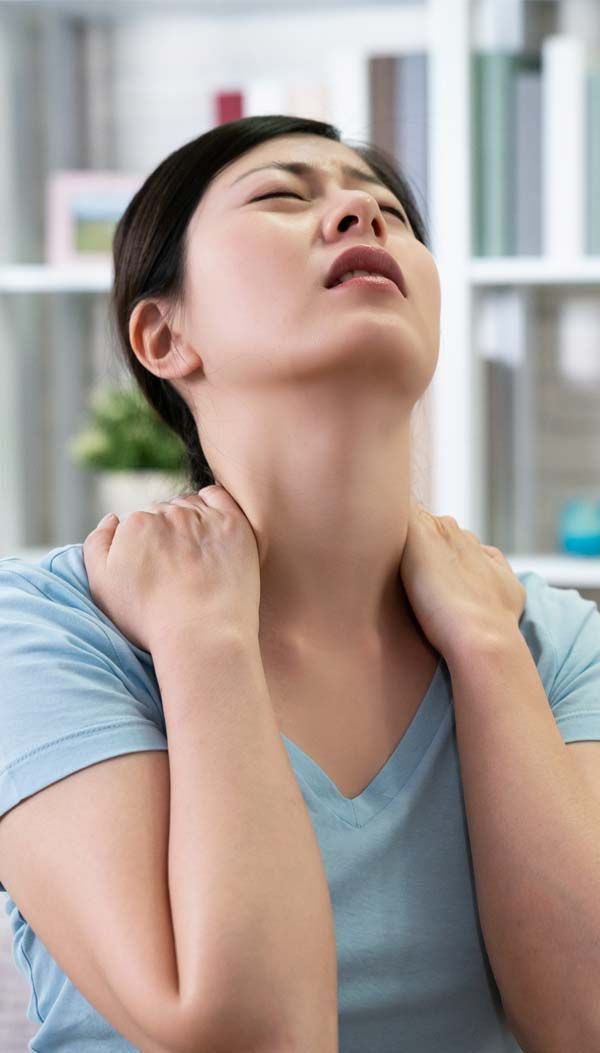 Woman with closed eyes massages her neck, indicating pain. She wears a blue shirt indoors, with a bookshelf visible in the background who has to Discover Effective Shoulder Pain Relief with Acupuncture Expertise by Marc Bystock, NYC Acupuncturist in Midtown Manhattan, NY 10016