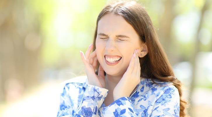 Woman outside, eyes closed, holding her ears, appearing to be in pain, needing TMJ Treatments NYC by Marc Bystock L.Ac.
