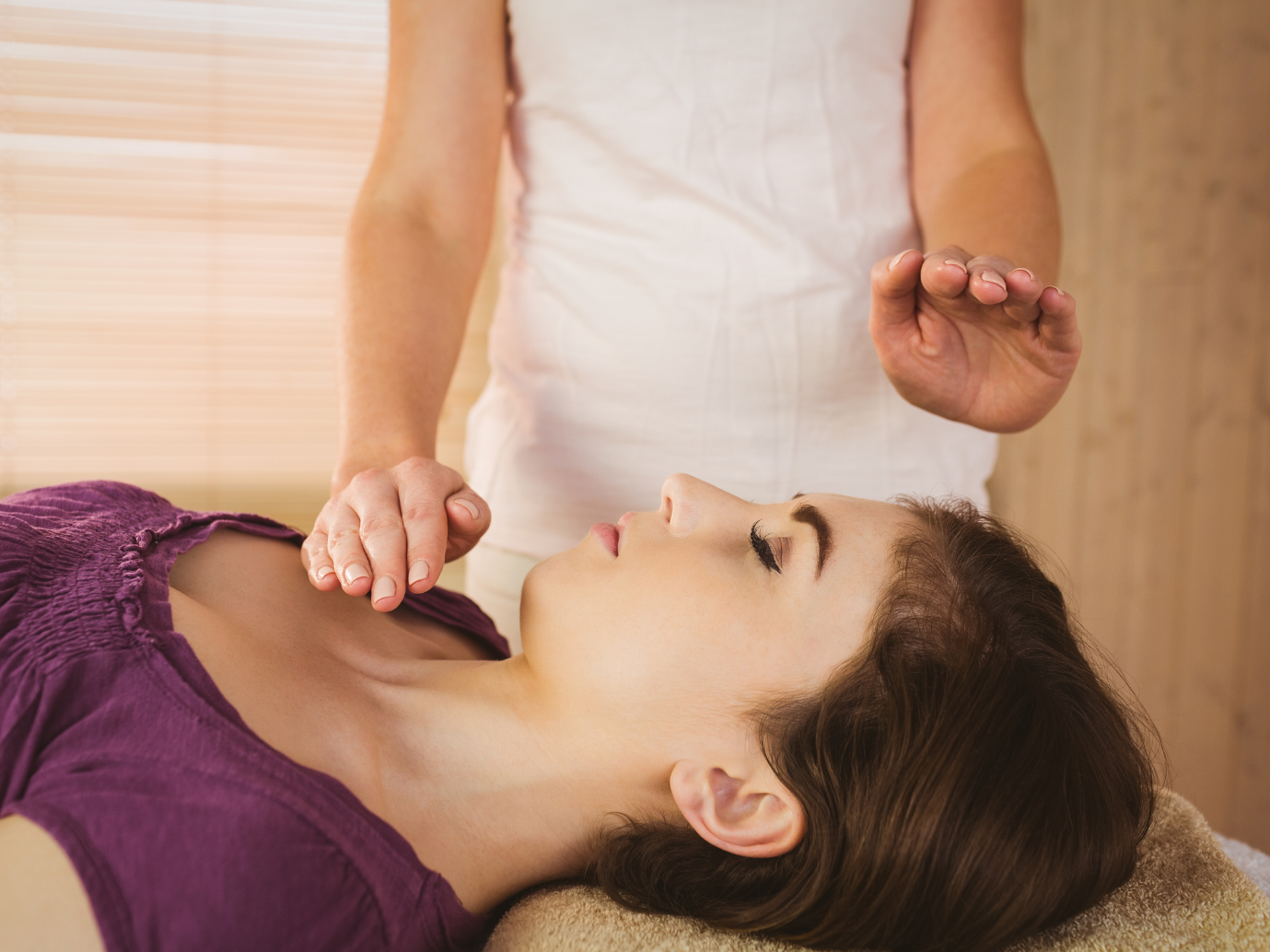 Woman receiving Reiki treatment: hands hovering over her body, eyes closed, serene expression.