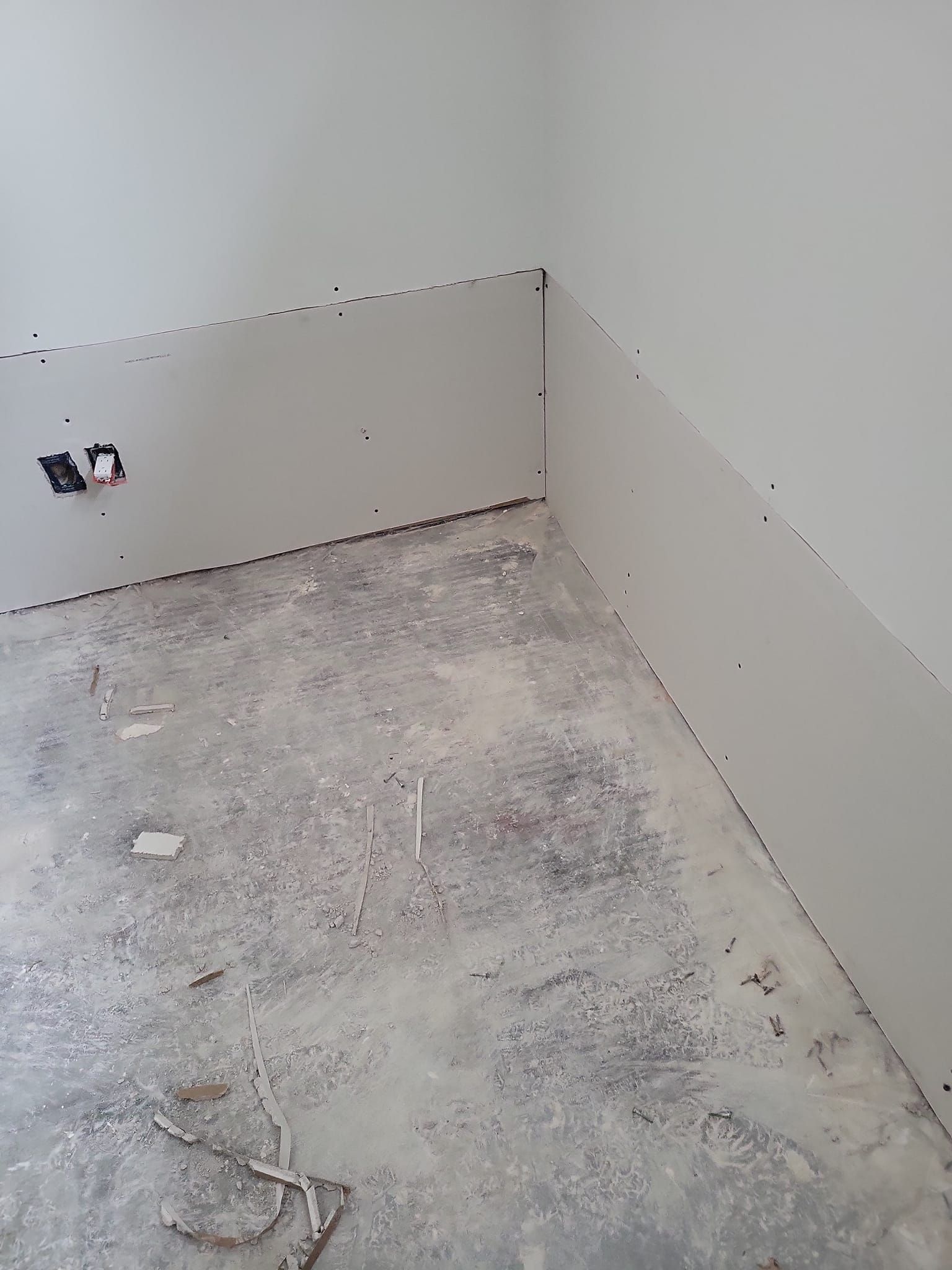 Un coin d'une pièce avec un sol en béton et un mur blanc.