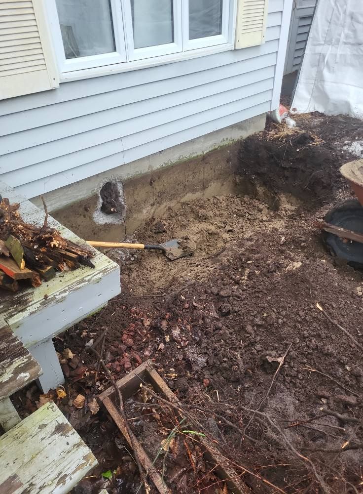 Une pelle est posée dans la terre devant une maison.