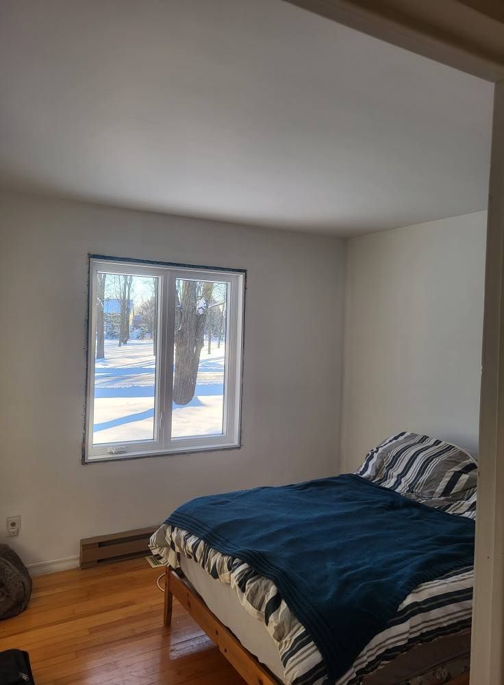 Une chambre avec un lit, une fenêtre et du parquet.
