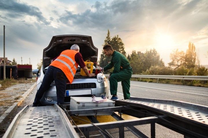 Two workers loading equipment onto a flatbed truck at sunrise beside a road