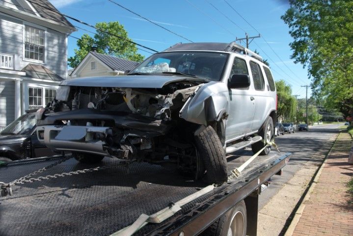 Wrecked white SUV on a tow truck in a residential street, front end heavily damaged.