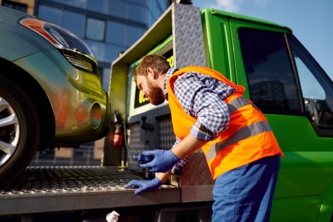 Tow truck driver in orange vest loading a car onto a green tow truck platform