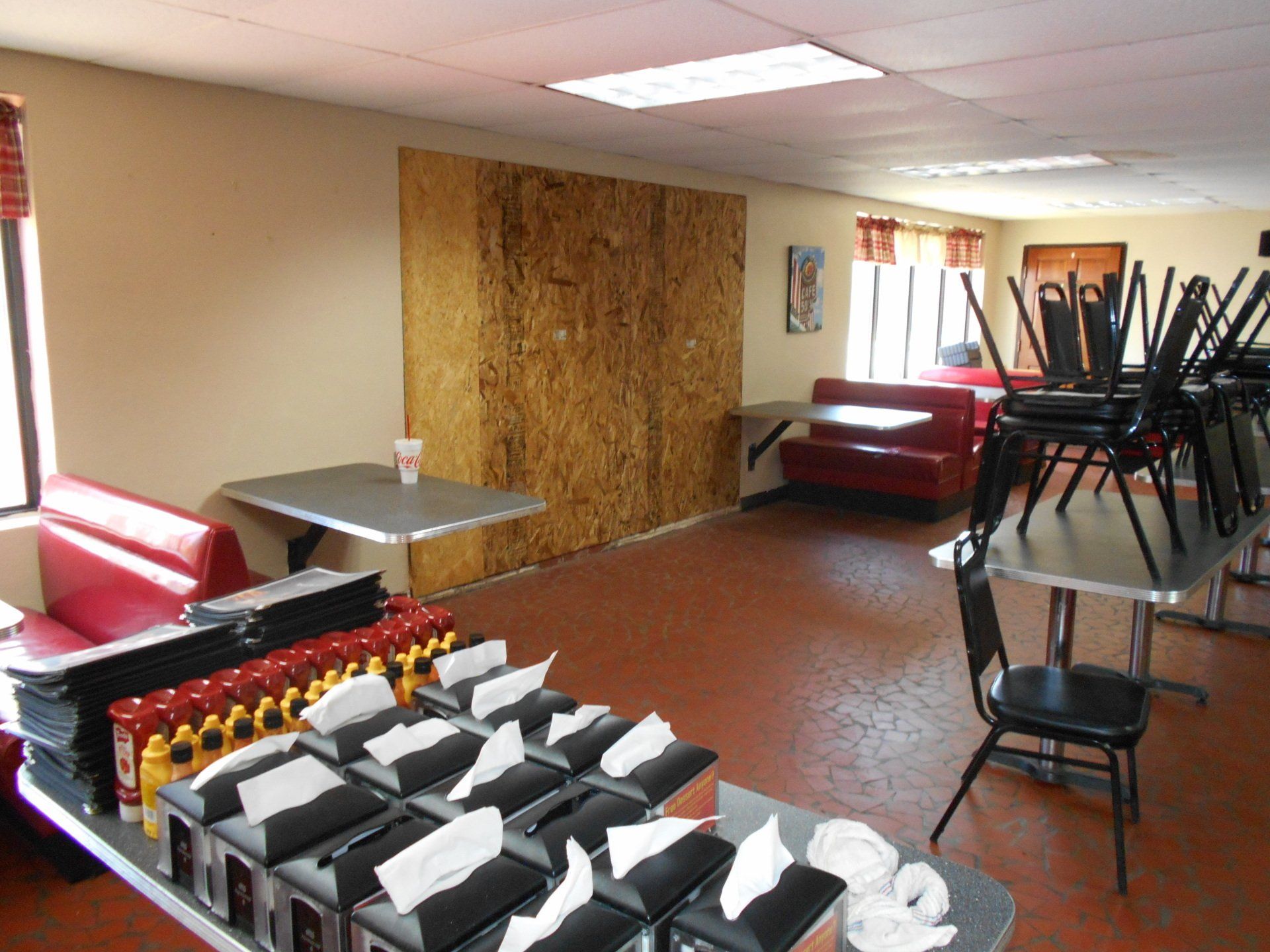 Empty diner interior: red booths, tables with napkins and condiments, chairs stacked, unfinished wall.