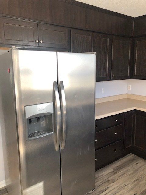 Stainless steel refrigerator in a kitchen with dark brown cabinets and light countertops.
