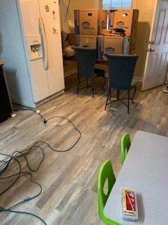 Kitchen with boxes, two chairs, a refrigerator, and a table with green chairs. A pack of cigarettes is on the table.