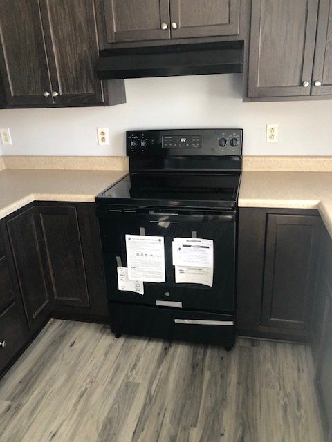 Black electric range in a kitchen with dark brown cabinets and light countertops.