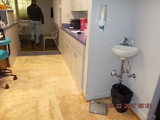 Interior of a room, featuring a sink, cabinets, a person walking, and a trash can.