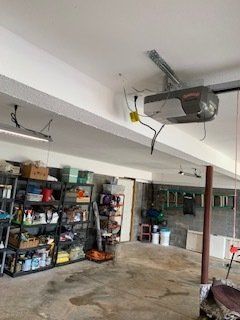 Garage interior with garage door opener, storage shelves, and concrete floor.