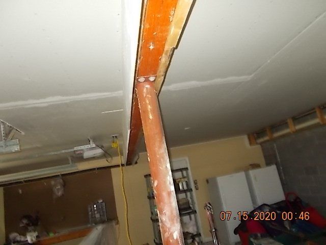 Support beam in a garage, orange wooden beam supports a brown pole, white ceiling and walls.
