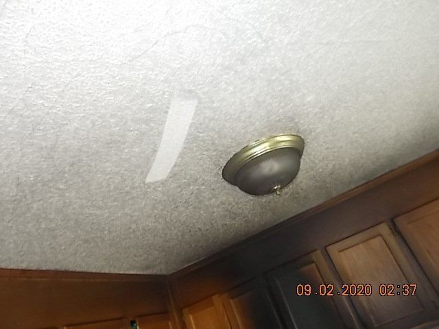 Ceiling with a light fixture and tape strip. Brown cabinets at the bottom.