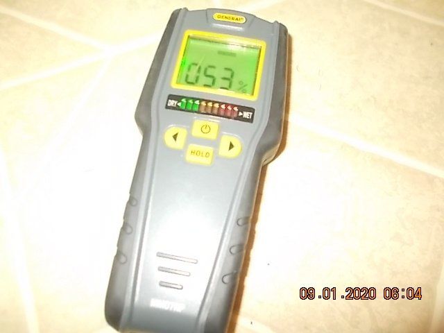 Moisture meter showing a reading of 0.53%. The device is gray and yellow with a green display.