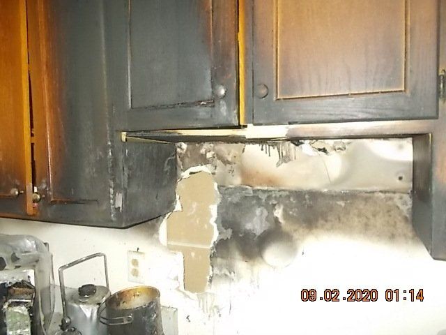 Burnt kitchen cabinets and wall, smoke damage, likely from a kitchen fire.