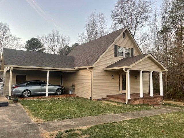 Tan house with a covered carport holding a silver car and a porch with white columns.