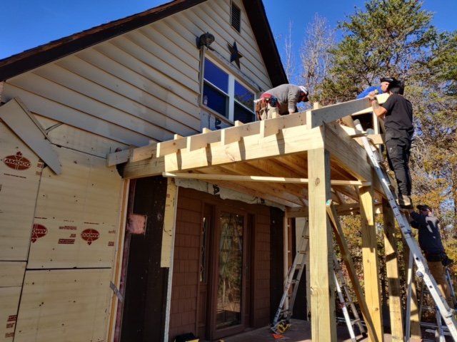 Construction workers building a wooden porch on a house with white siding.