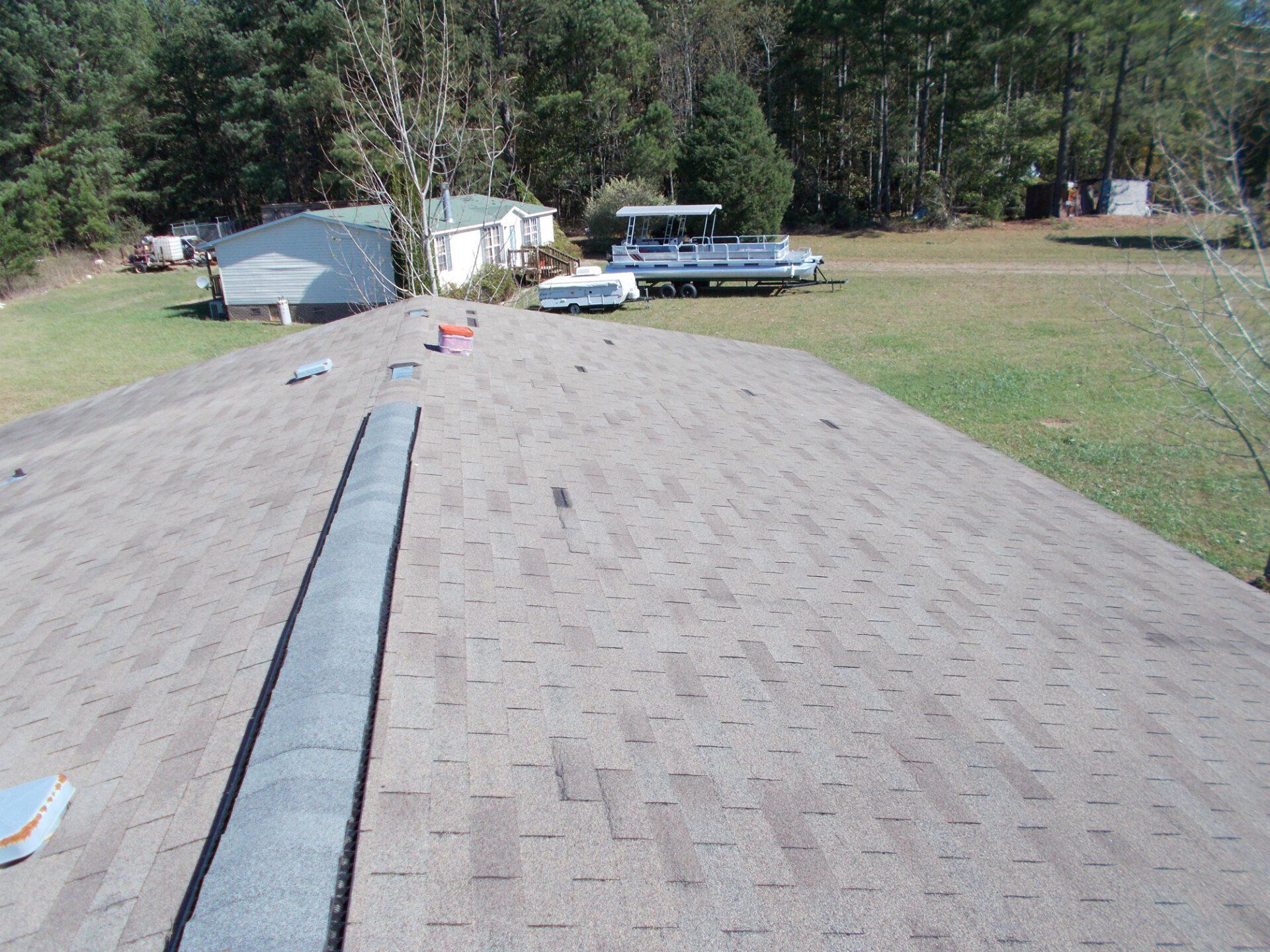 A brown shingle roof with a gray flashing strip. Trees and a mobile home are in the background.