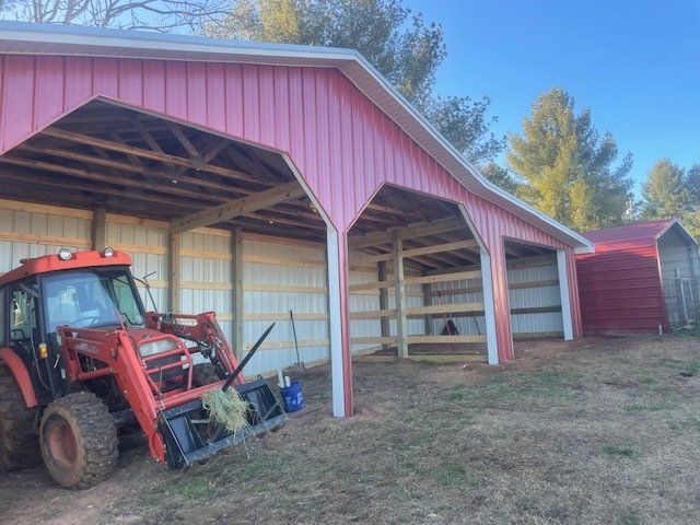 Red tractor parked under a pink and white barn with stalls; small red shed nearby.