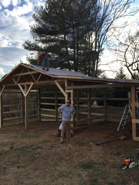 Men building a wooden shed, with roof partially completed. Outdoors, grassy area.
