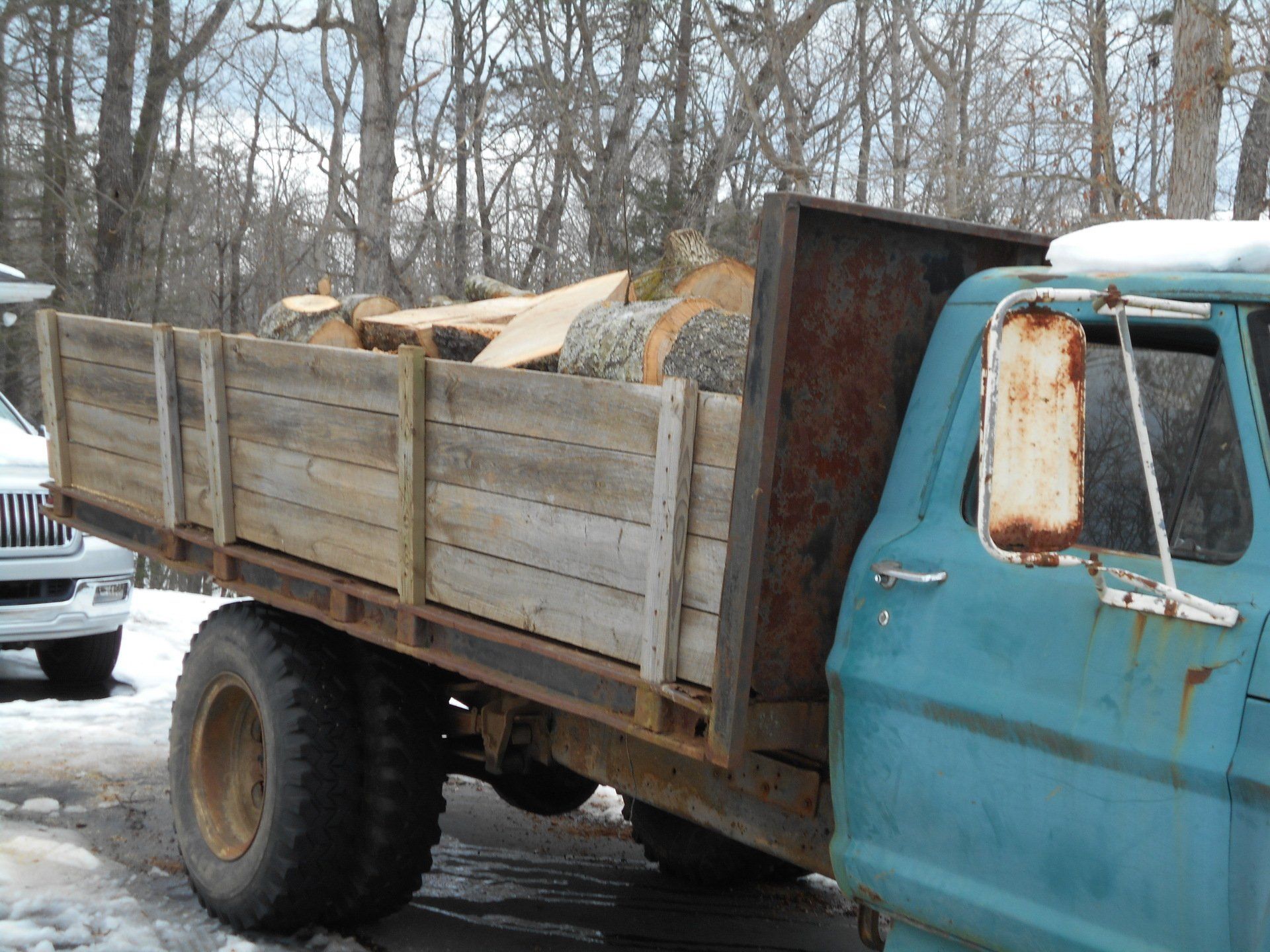 Blue pickup truck bed loaded with firewood in a snowy outdoor setting.