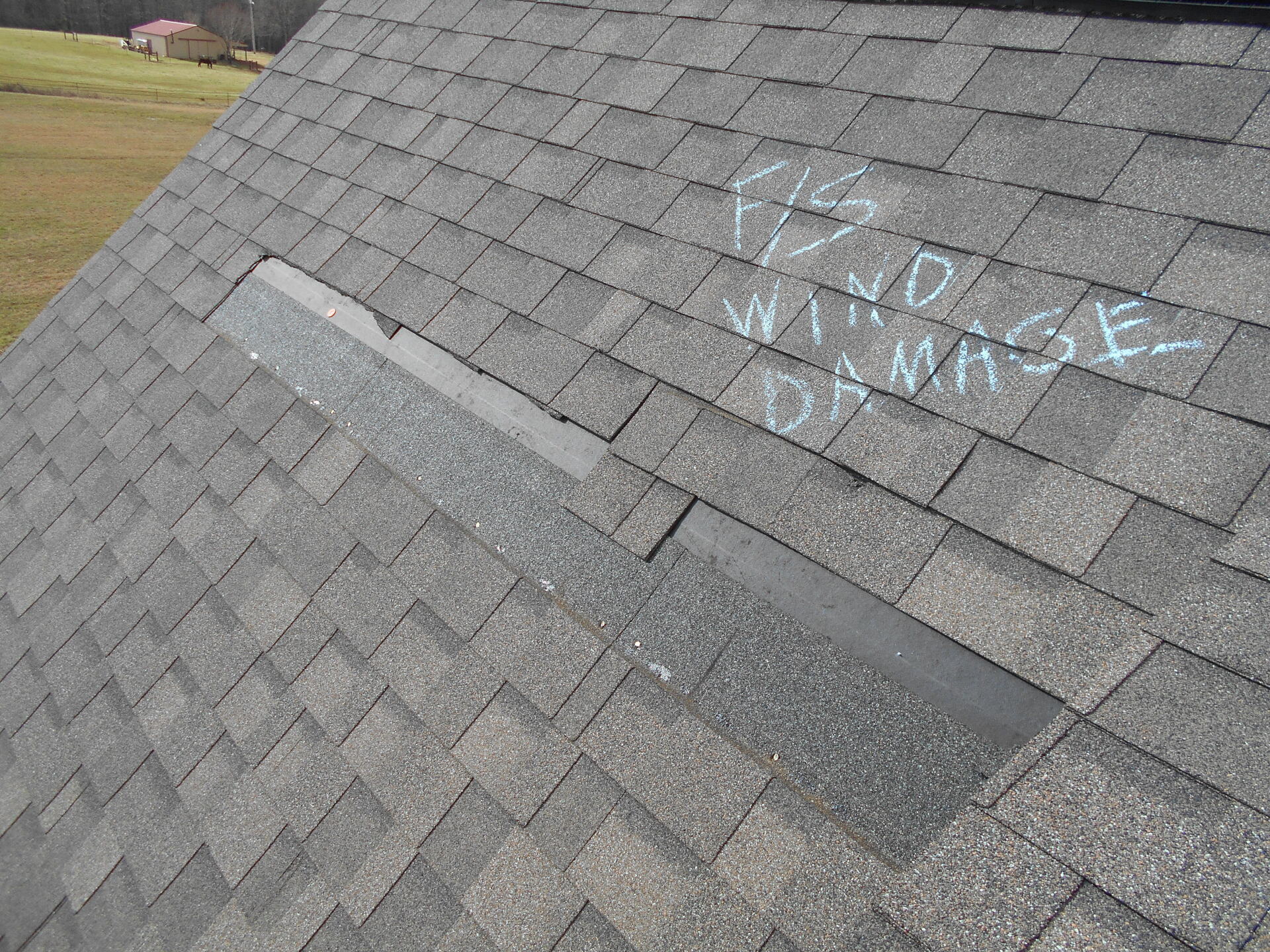 Close-up of a shingled roof with a marked section. Chalk writing: 