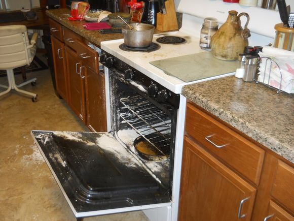 Open oven covered in white powder, next to a messy stovetop and counter.