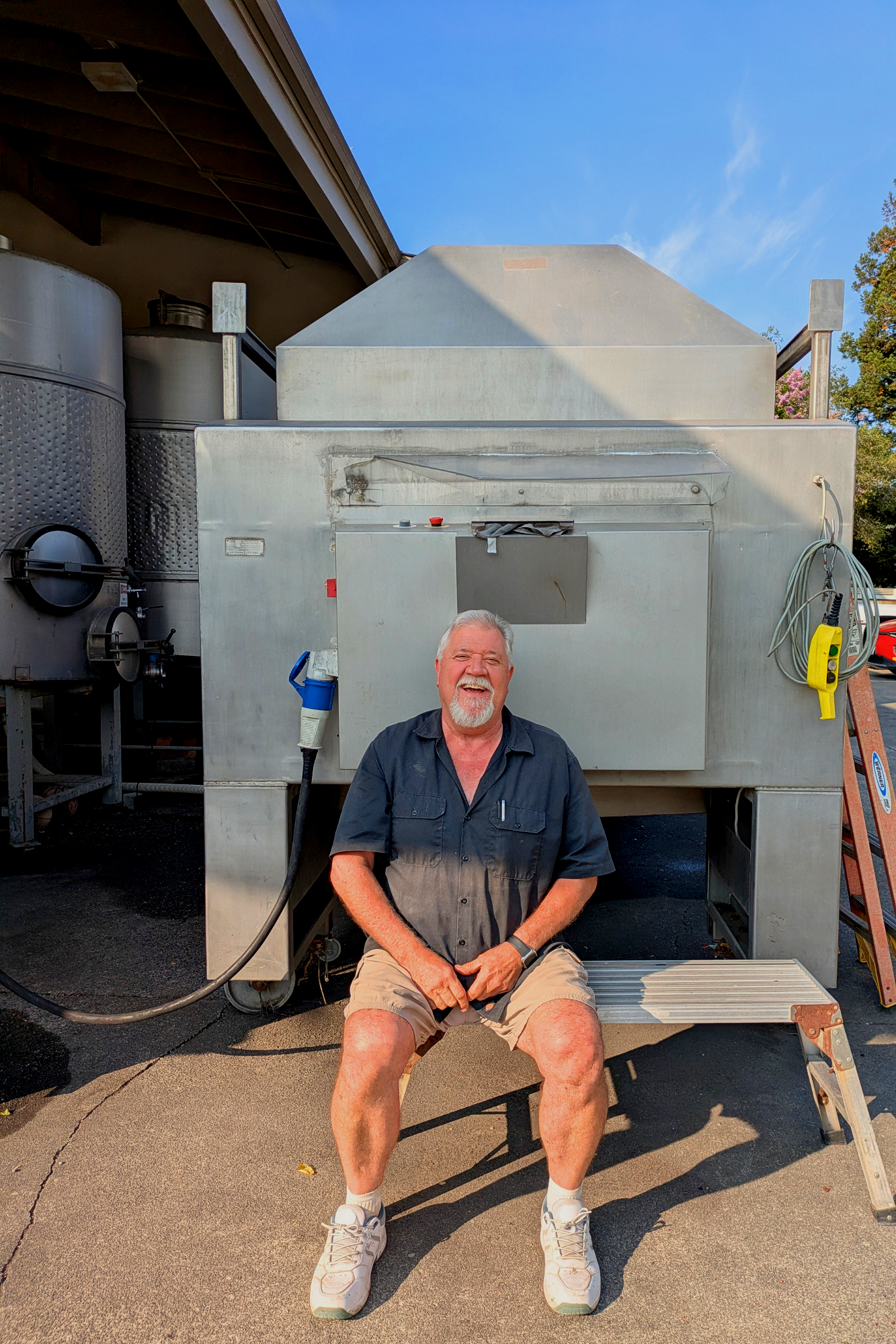 Man sitting on a bench in front of a large industrial machine outdoors under a blue sky
