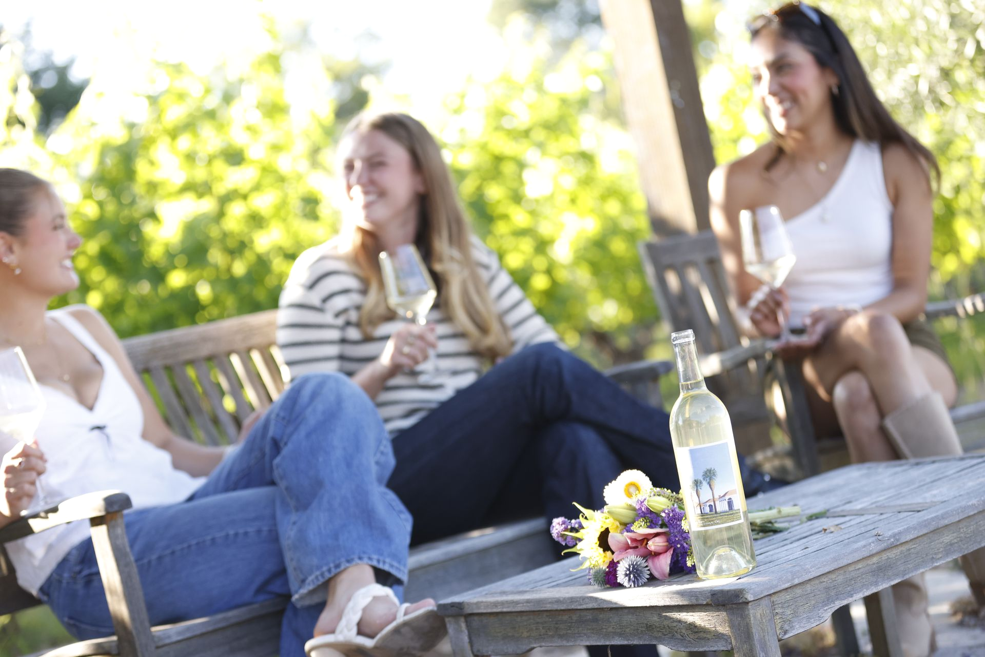 Three people chatting outdoors on a patio with drinks, seated around a table in sunlight