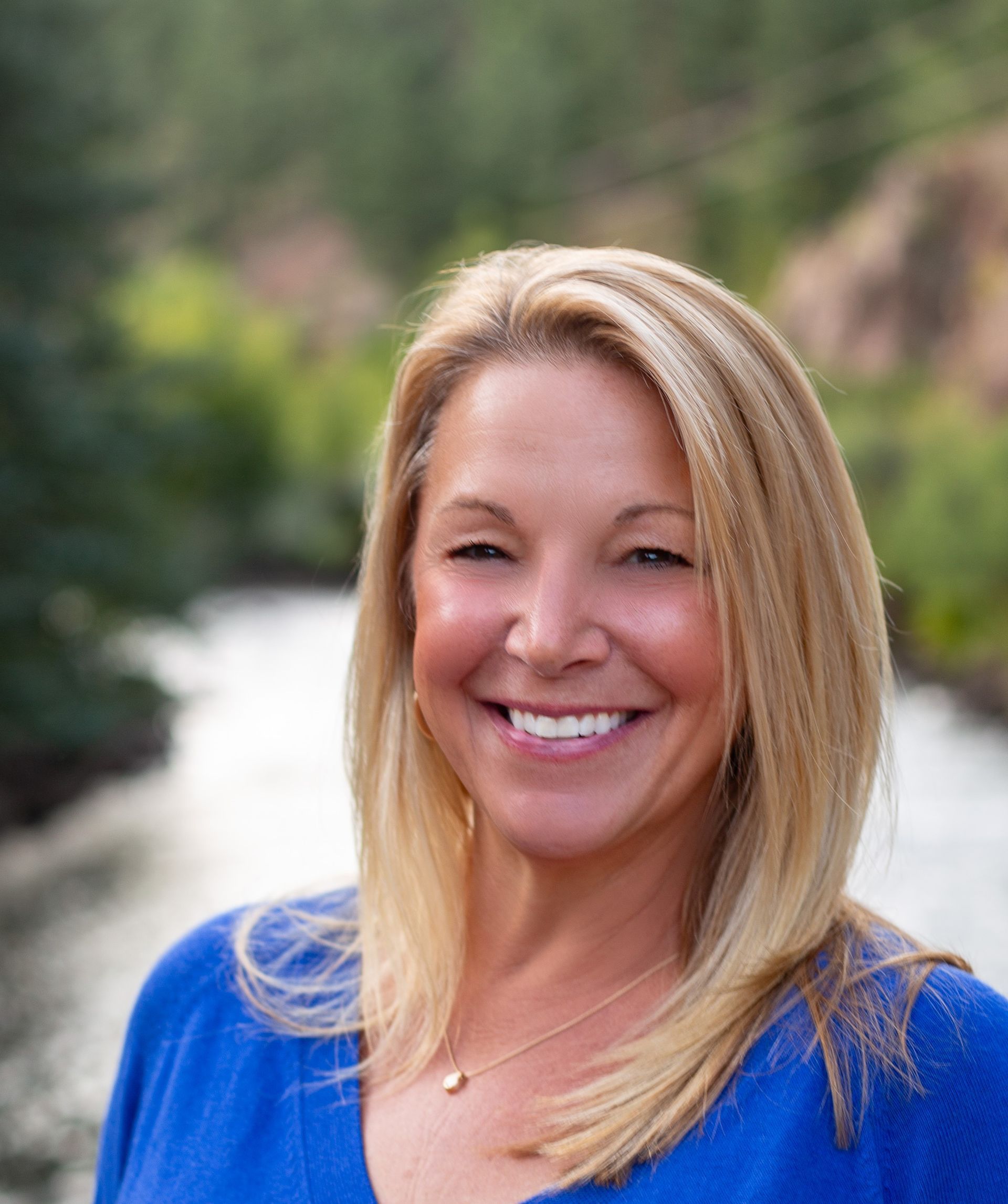 Smiling woman in a blue top outdoors with a blurred natural background