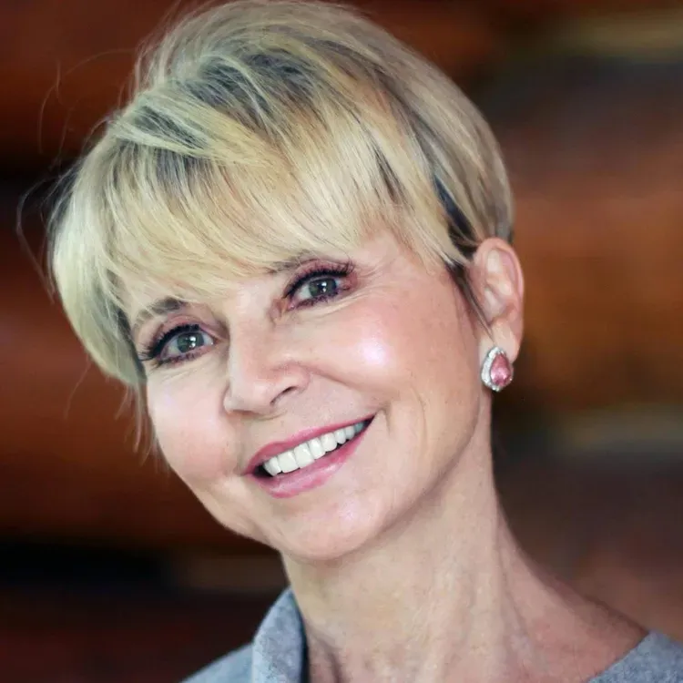 Smiling woman with short blonde hair and pink earrings against a blurred warm background