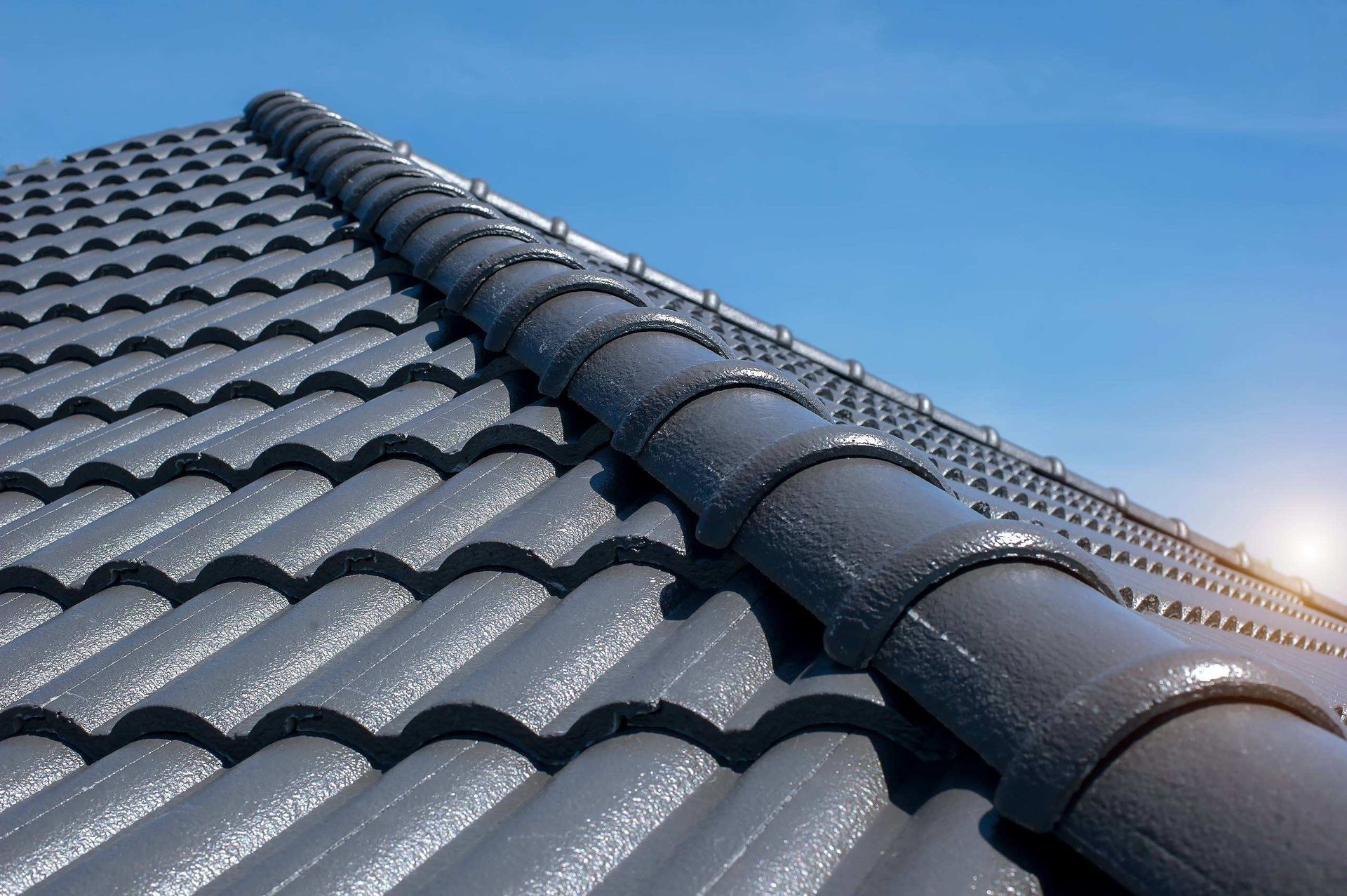 Dark Gray Tiled Roof with A Central Ridge Line Against a Blue Sky at Sunset — Goonellabah Roof Tilers In Northern Rivers, NSW