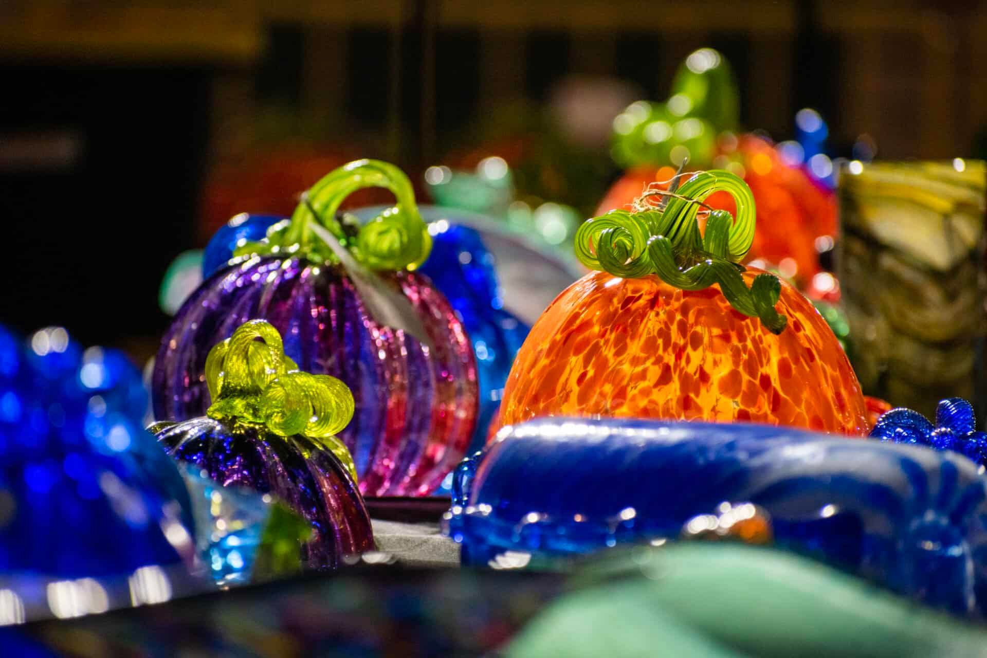 Colorful glass pumpkins with green stems displayed in a row, including purple and orange pieces.