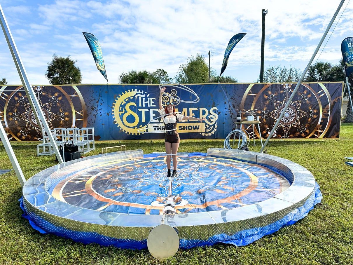 Woman standing on a circular stage at The Traitors game show set, with blue and gold backdrop and streamers.