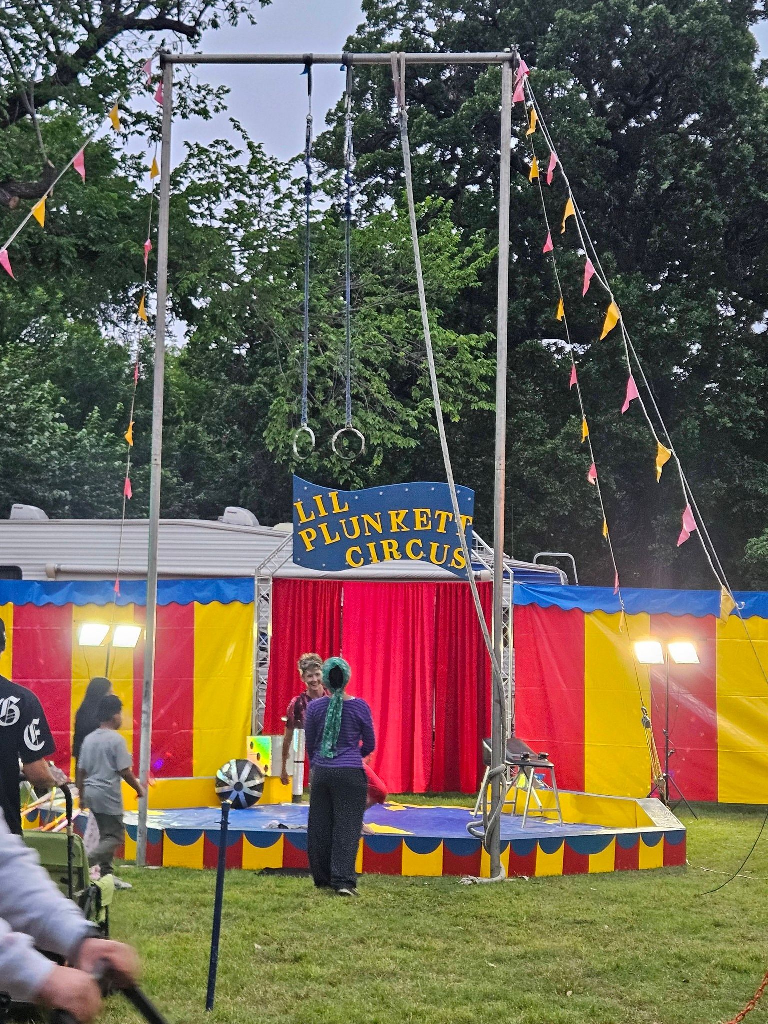 Colorful playground circle ride at an outdoor fair, with bunting, red curtains, and children nearby
