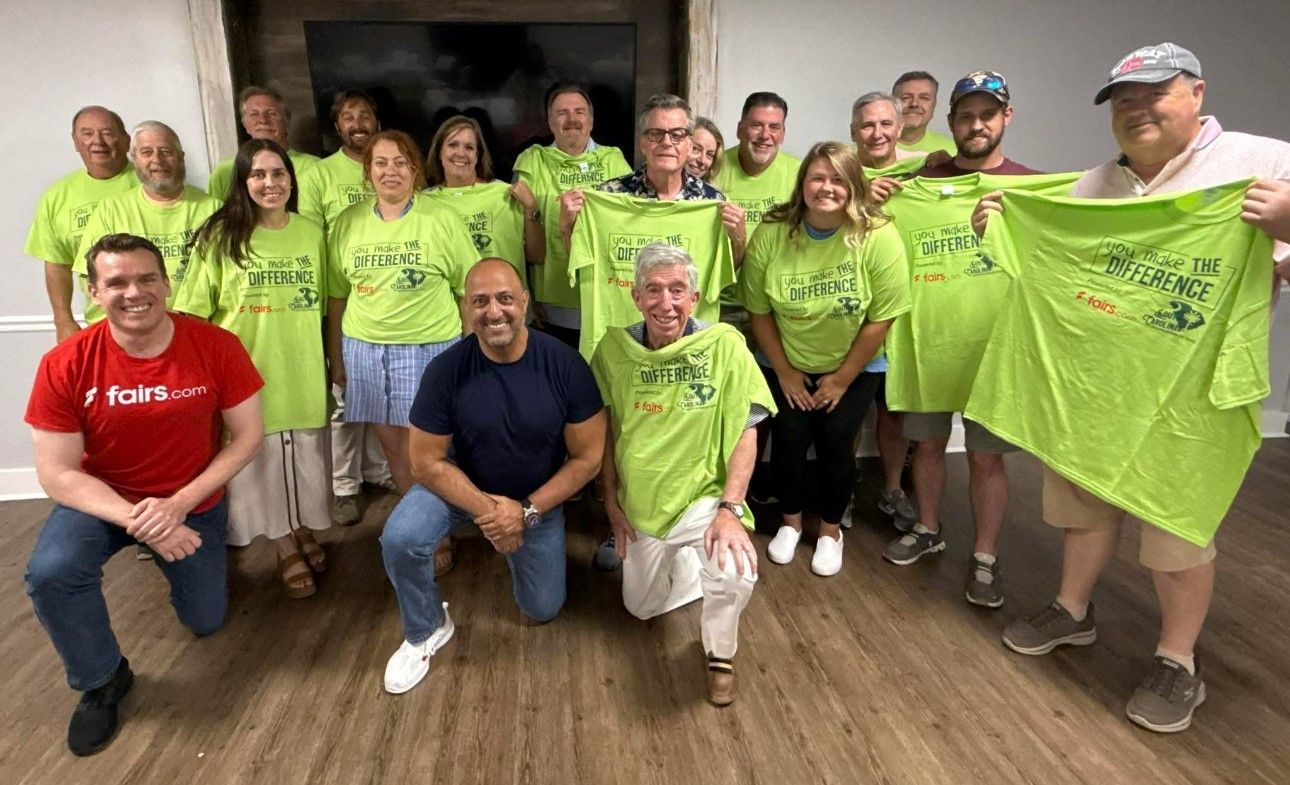 Group of smiling people in bright green shirts posing indoors, holding up shirts and wearing casual clothes