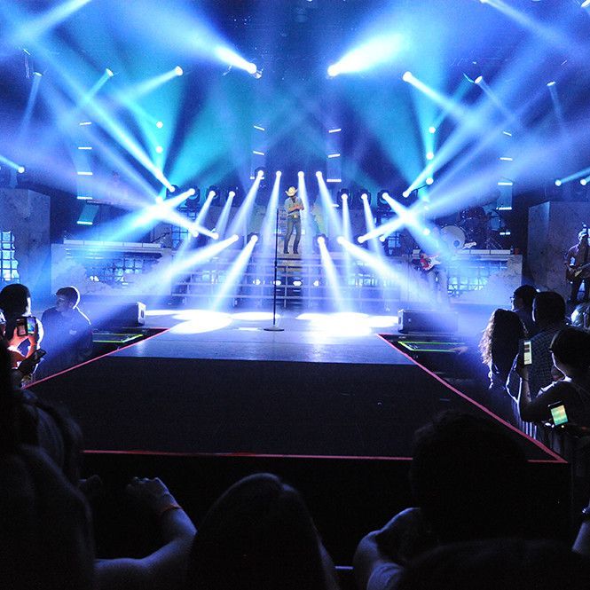Concert stage with blue spotlights and a catwalk, seen from the audience