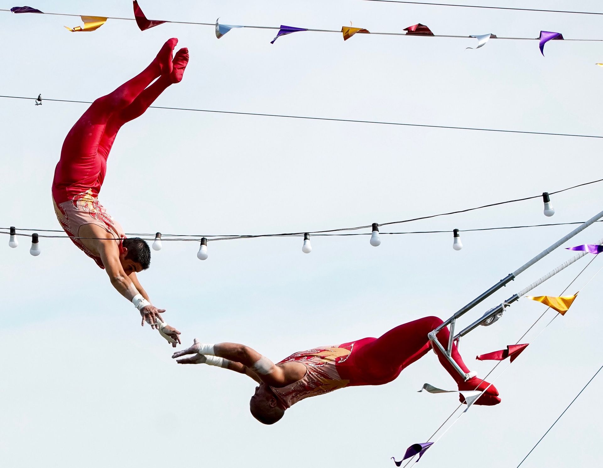 Two acrobats in red costumes performing aerial trapeze stunts against the sky