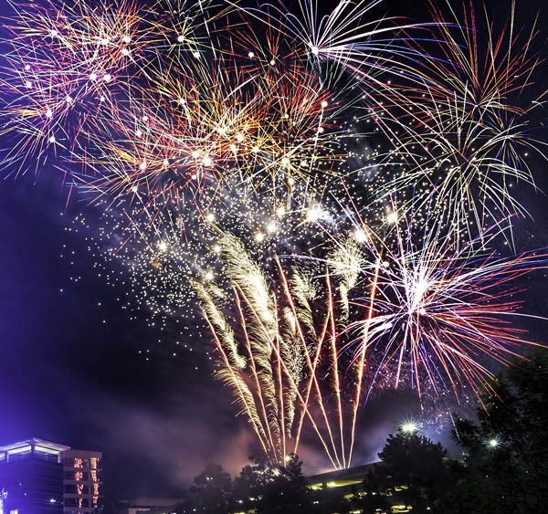 Colorful fireworks bursting over a nighttime skyline, lighting up the sky with red, white, and gold trails