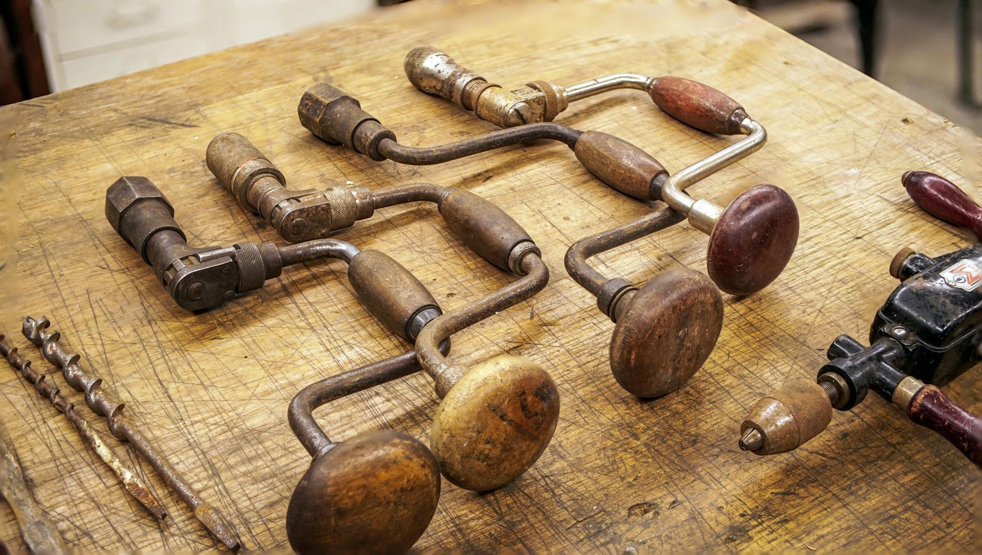 Assorted antique hand drills with wooden handles arranged on a worn wooden surface