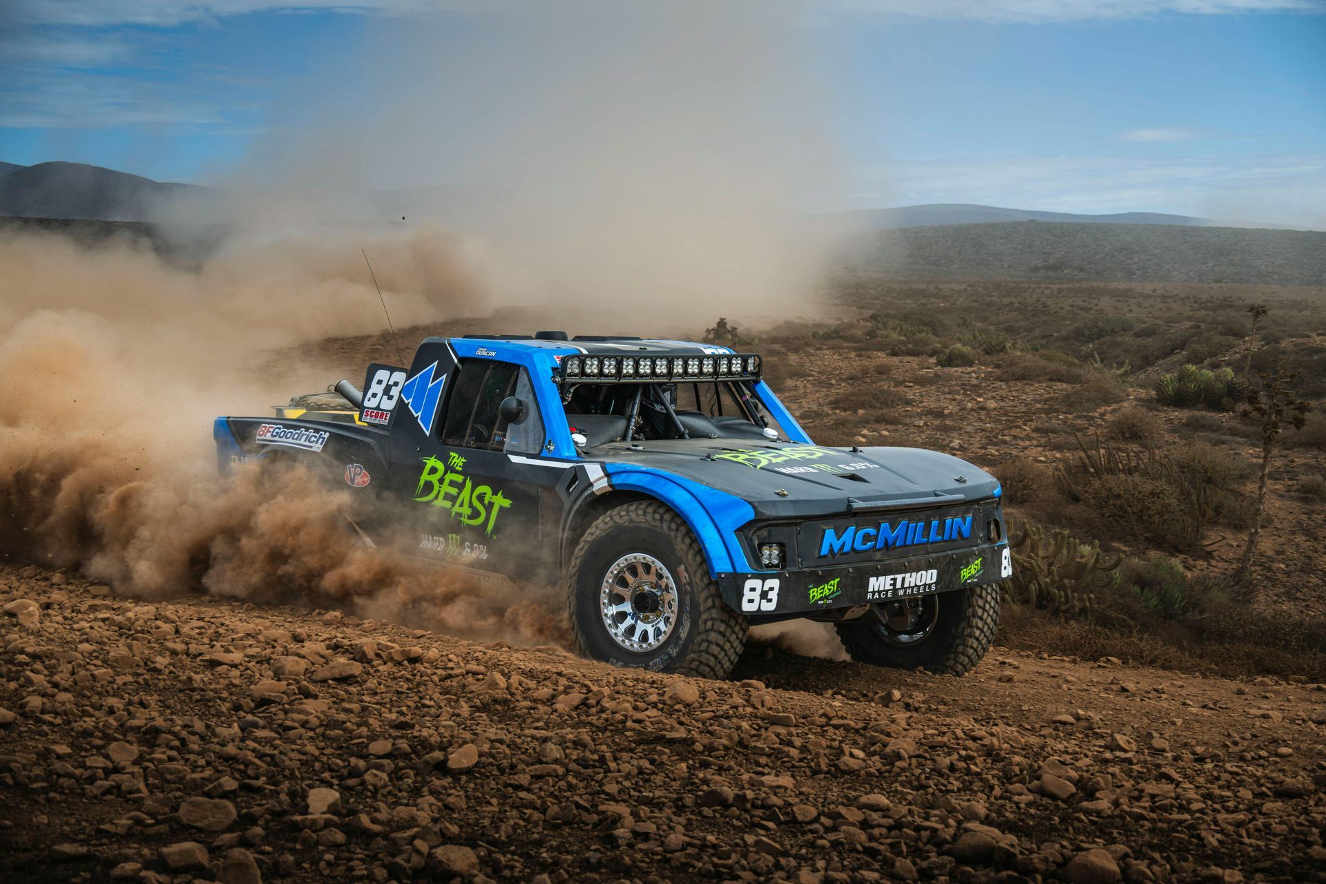 Blue off-road race truck kicking up dust on a rocky desert track