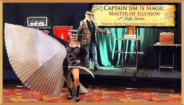 Magician on stage in black costume with giant silver fan prop, beside banner reading “Captain Jim is Magic”