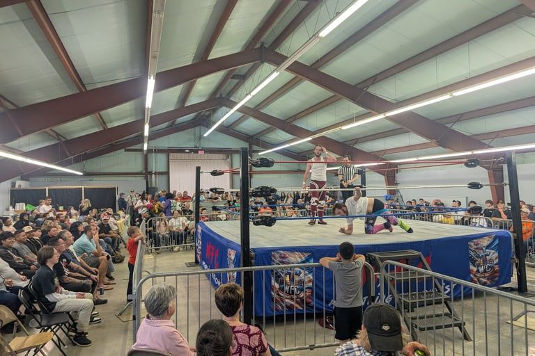 Wrestling match in a packed indoor gym, with spectators seated around the ring.