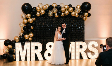 Wedding couple with MR & MRS light-up letters, black and gold balloons and sequin backdrop
